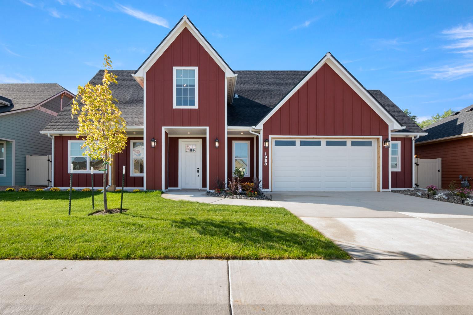Front view of the Wellness Home from the Parade of Homes, featuring a red exterior, tall roof, and landscaped green yard. 